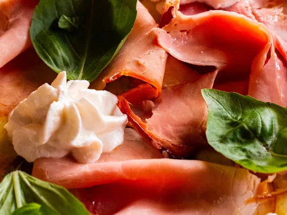 Primo piano di prosciutto cotto arrosto, ciuffi di ricotta di bufala e basilico