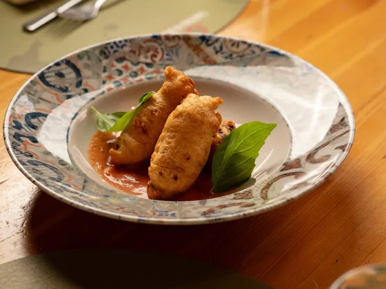 Fiori di zucca fritti serviti in un piatto di ceramica decorata, su crema di datterini
