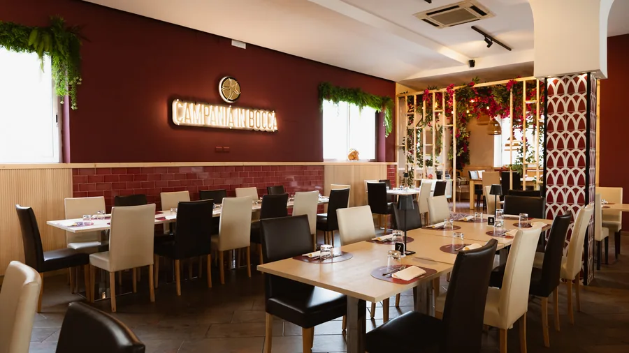 La sala della pizzeria: pareti bordeaux, boiserie chiara, l'insegna luminosa Campania in Bocca e i tavoli apparecchiati
